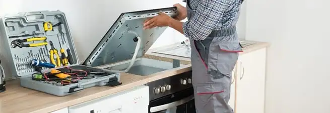 Cooktop repair technician lifting a built-in stovetop for service in Rochester, NY