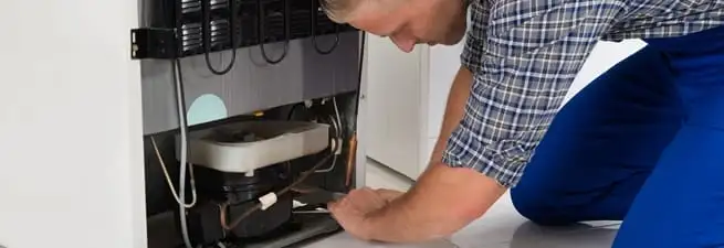 Refrigerator repair technician servicing the compressor and condenser area in Rochester, NY