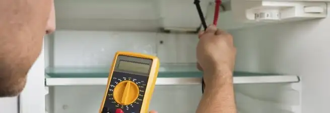 Refrigerator repair technician testing electrical components with a multimeter in Rochester, NY