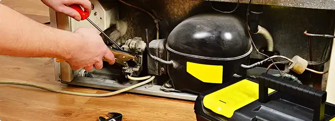 Refrigerator repair technician fixing the compressor and wiring in Rochester, NY